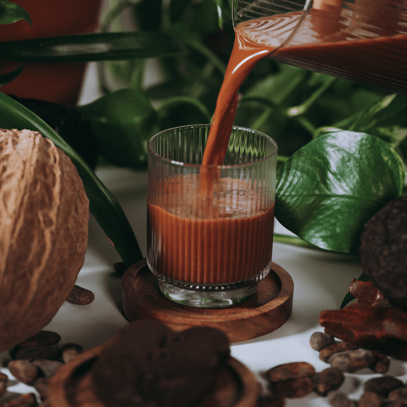 A mug of ceremonial cacao freshly poured, surrounded by cacao pods and walnuts